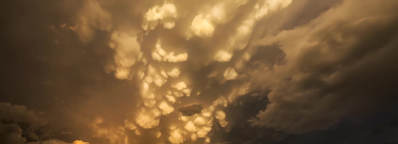 Mammatus clouds with a distinct pouchlike structure are illuminated by a warm golden sunset lightthe sky displays a dramatic texture as the rounded cloud formations shift and churn under the changing light