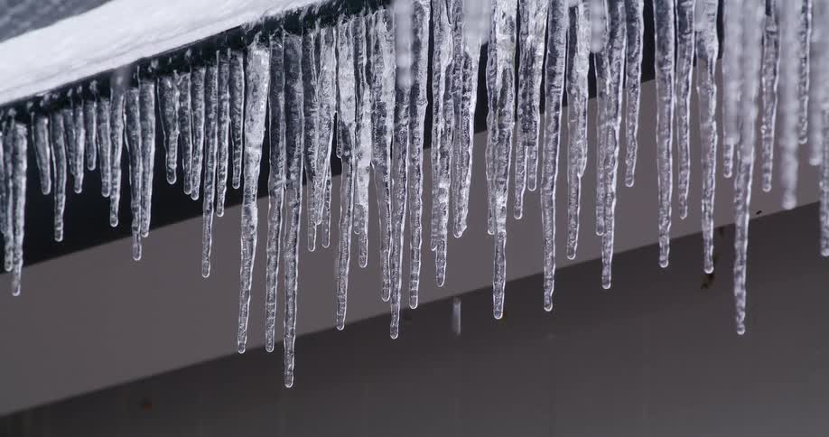 Icicles melt on the edge of a rooftop while it rains