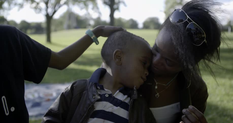 A woman sits on a blanket in the park with two boys