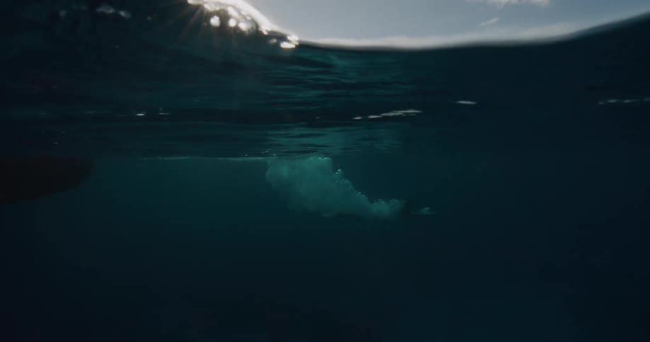 A silhouetted person dives off the side of a boat into the ocean at sunset with sunlight reflecting across the water