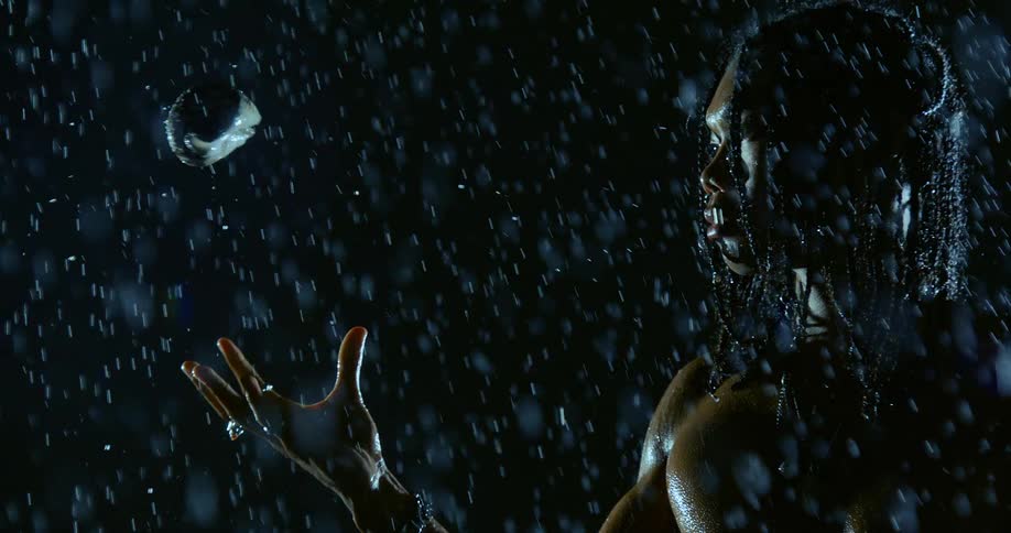 Person with braids tosses a shell into the air under heavy rain against a dark background
