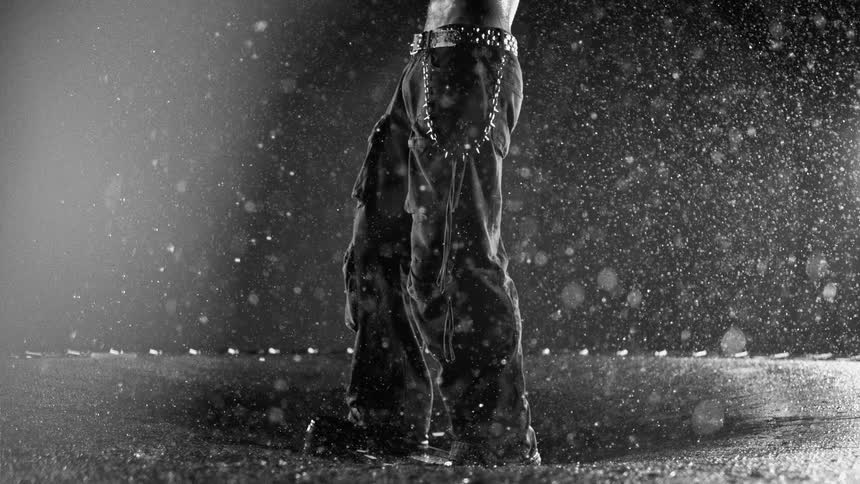 Legs wearing loose pants under heavy rain with visible droplets in the air and on the wet ground