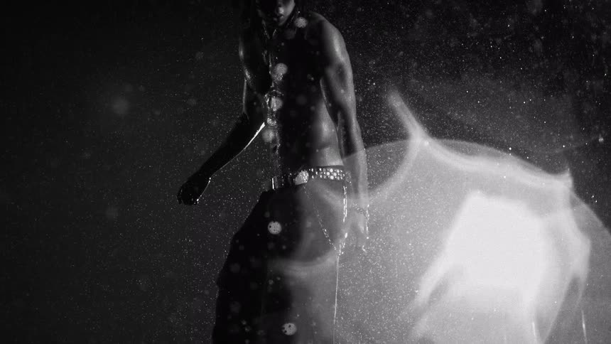 Shirtless man under heavy rain with side lighting and visible water particles