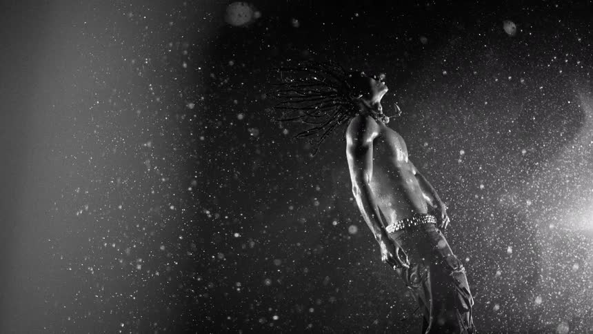 Man wearing a metallic belt flings his braided hair back while standing at night under the rain