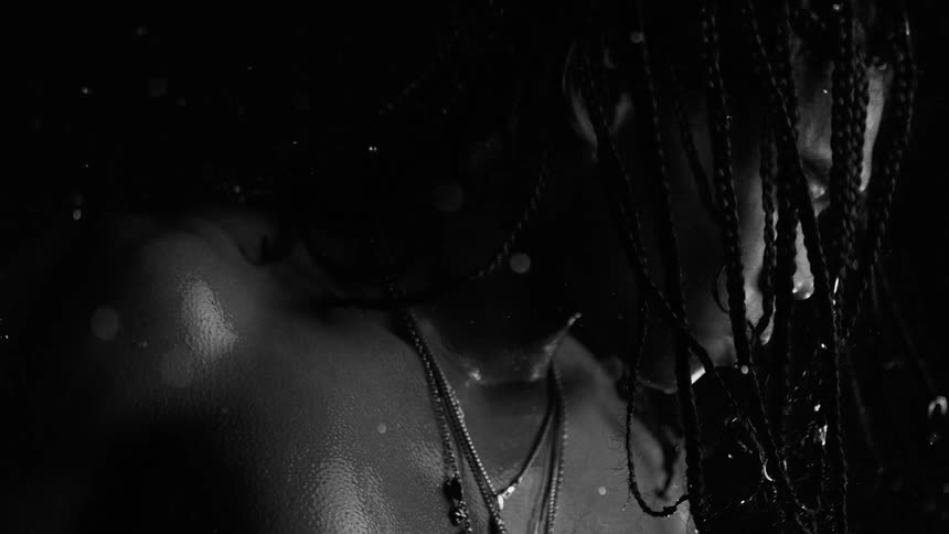 Hair braids over the face of a man looking down as rain falls