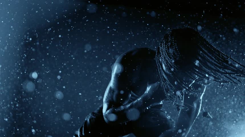 Hair braids flow through the air as a man bends outdoors at night under the rain