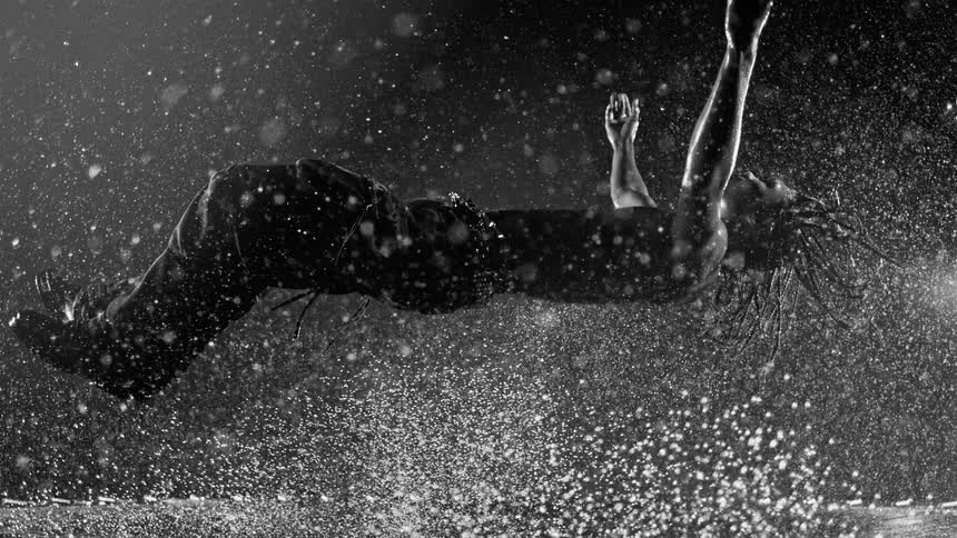 Man performs a horizontal jump under heavy rain with water particles scattered around