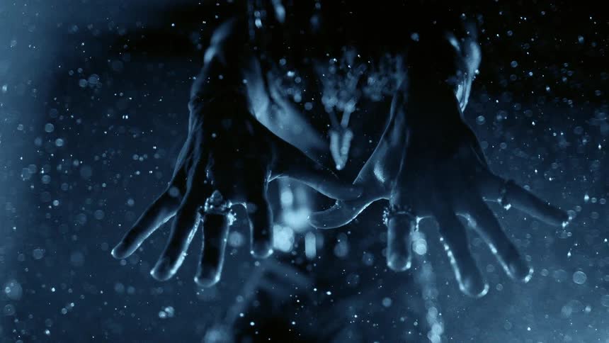 Outstretched hands under heavy rain with blue lighting and droplets suspended in the air