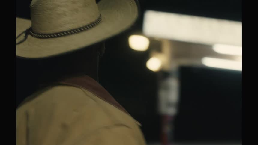 A man wearing a cowboy hat and jacket is seen in profile at night