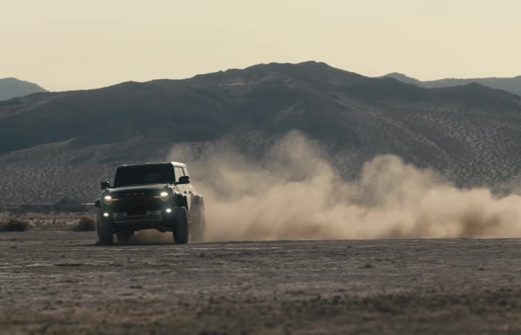 Person drives their vehicle in circles creating a cloud of dust near foggy mountains