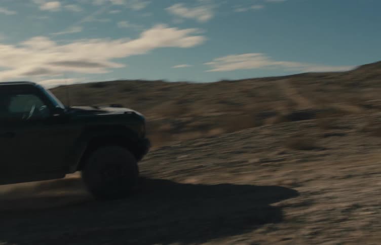 Utility vehicle drives fast on a dirt road kicking up dust under a partly cloudy sky