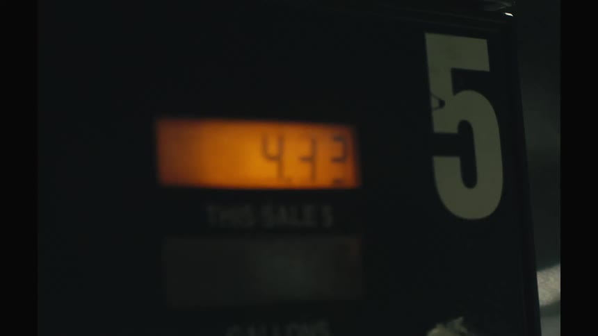 A close view shows the digital display on a gas pump as the cost and gallons quickly increase during a sale at night
