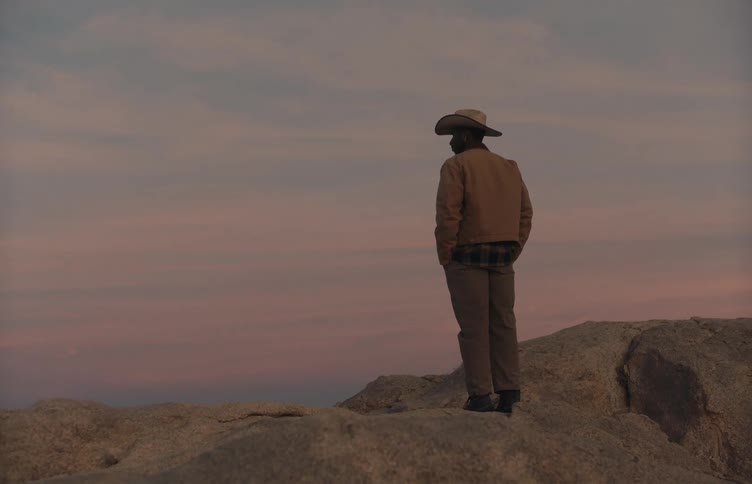 A man wearing a cowboy hat stands atop a mountain ridge