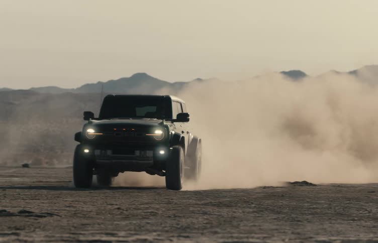 A person drives a jeep very fast and takes a hard turn across a dusty plain