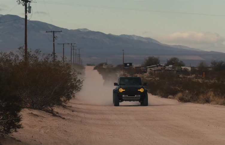 A rugged suv drives down a dusty desert road lined with utility poles with mountains rising in the distance