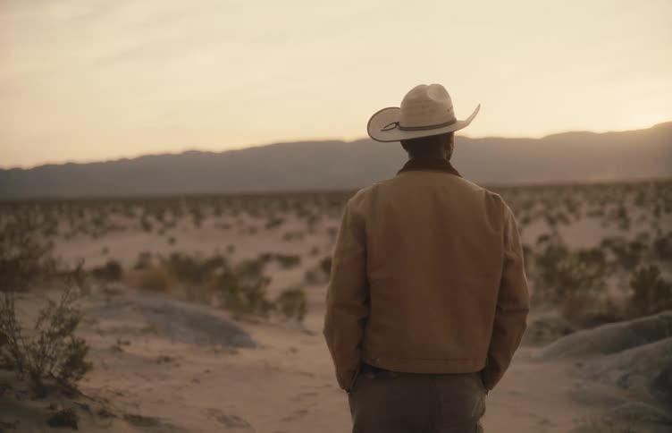 A man in a cowboy hat takes a few steps while standing in a desert at sunset