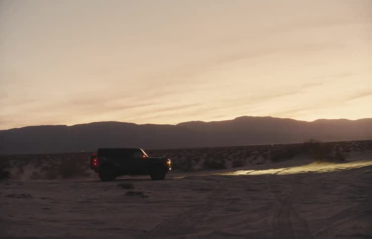 Utility vehicle drives along a desert trail at dusk with mountains in the background