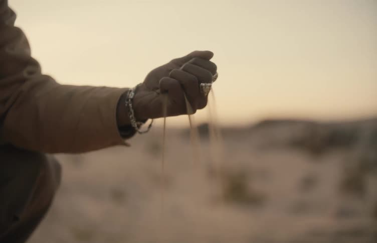 Hand holds sand slipping through fingers at sunset in a desert landscape