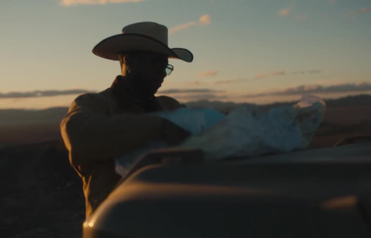 Man standing in front of his truck holding down a map on the hood and reading