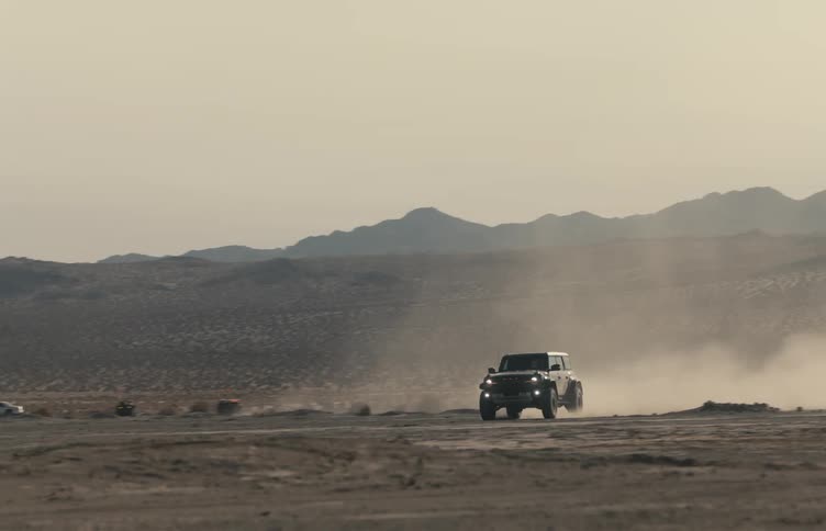 Jeep traveling fast through the desert leaving a trail of dust with mountains in the distance