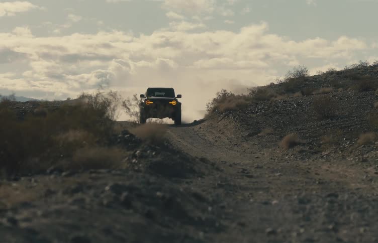 A jeep drives over a dirt road an takes a sharp turn which creates a cloud of dust
