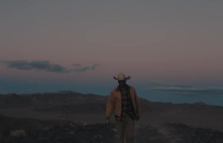 Man puts his hand on his cowboy hat as he walks away from the coast