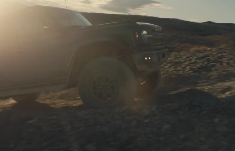 An offroad suv drives over rocky terrain in a rugged desert landscape illuminated by warm low sunlight