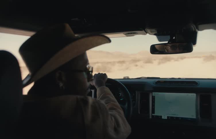 A man in a cowboy hat drives his jeep across a desert plain