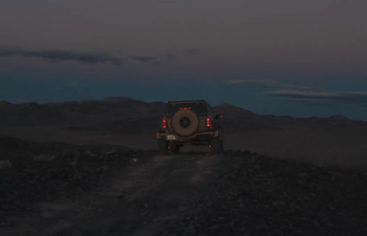 Utility vehicle climbs a rocky hill at dusk with rear lights on