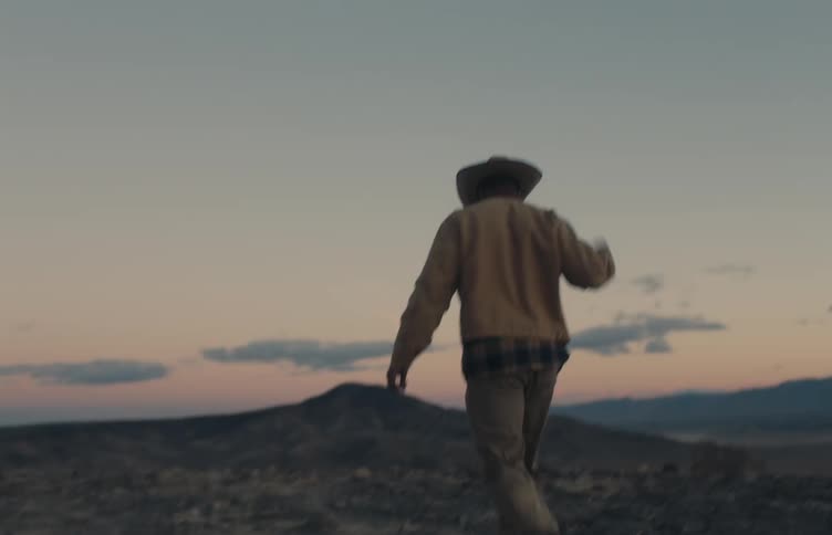 Man wearing a hat gets into a utility vehicle parked on rocky terrain at dusk