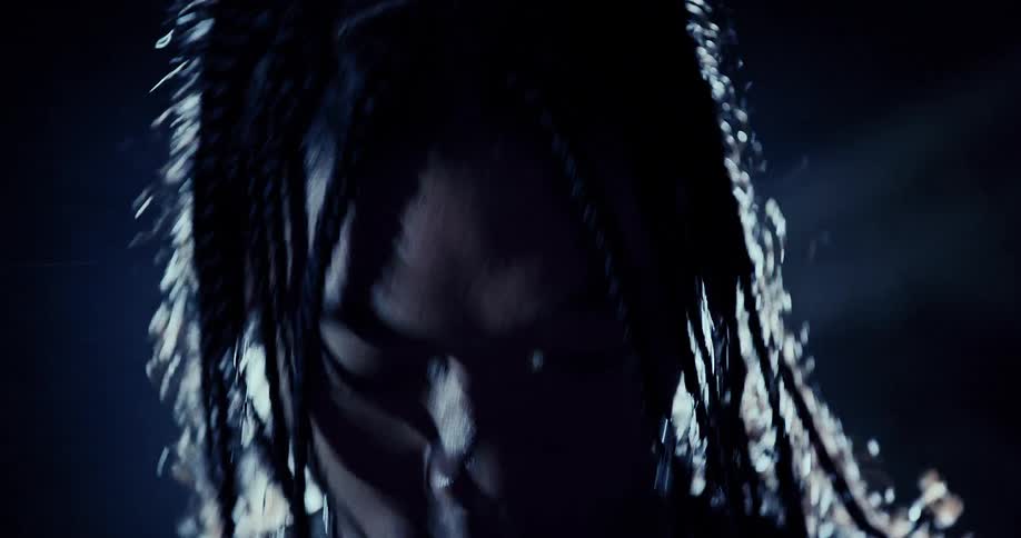 A man with braids wearing a mesh top stands in front of a spot light