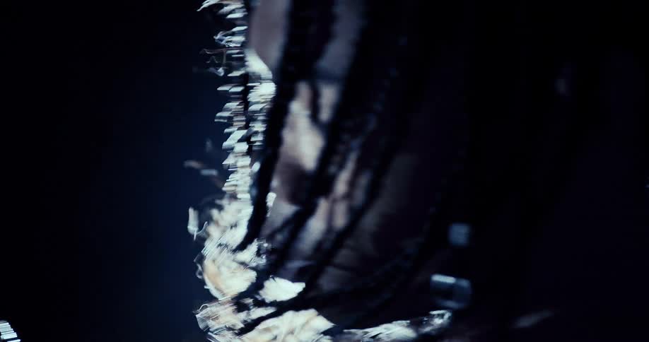 A closeup of a womans face with braided hair is illuminated by cool blue light highlighting water droplets and reflective details against a dark background