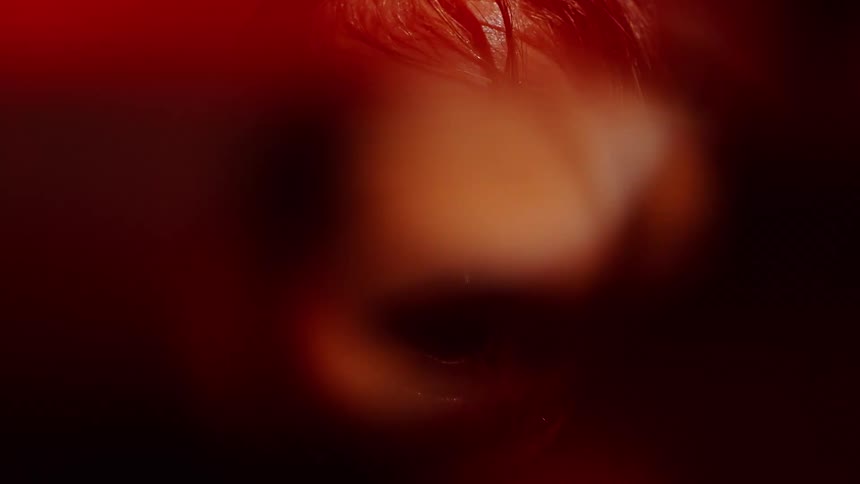 Female face with wet hair illuminated by intense red light against a dark background