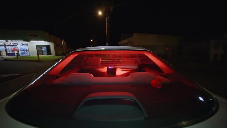 Rear interior of a car illuminated in red during a nighttime drive in an urban area