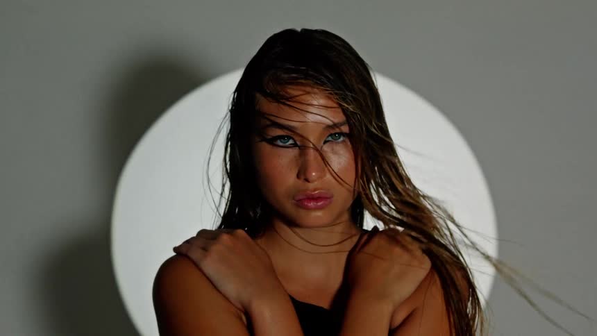 Woman with wet hair crosses her arms in front of a background with a white circle