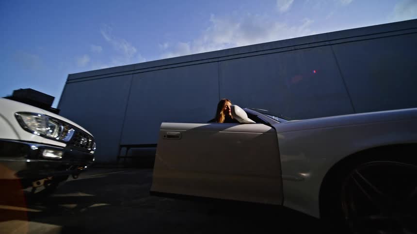 A woman exits a white car that is parked next to a pickup truck
