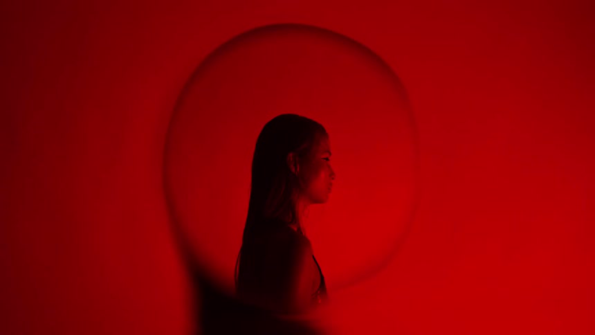 Young adult woman seen through the glass part of a light bulb in a room with red flashing lights