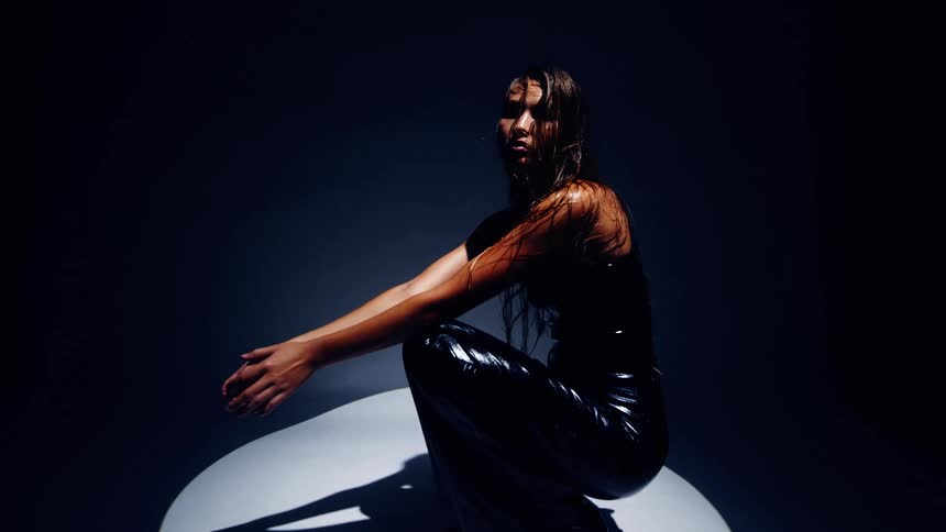 Woman sitting under a circular spotlight in a dark environment with arms extended