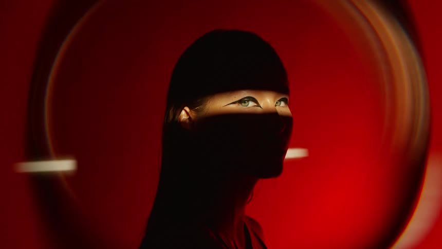 A womans silhouette is cast against a red background with a horizontal light beam briefly revealing her eyes