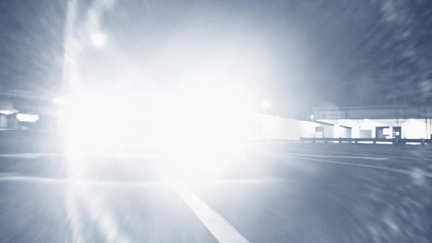 A toyota sedan driving down a street at night its headlights illuminating the road and surrounding area as it moves
