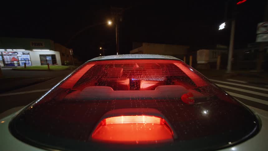 Rear of a car with red interior light during a nighttime drive at an urban intersection
