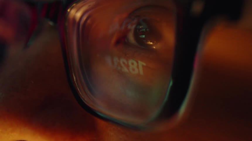 Adult man wearing glasses with a nervous facial expression staring at a screen with blurred flickering lights indoors