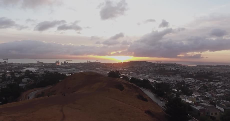 Aerial view of a hilltop with a valley below it and the sun setting behind the mountains in the distance