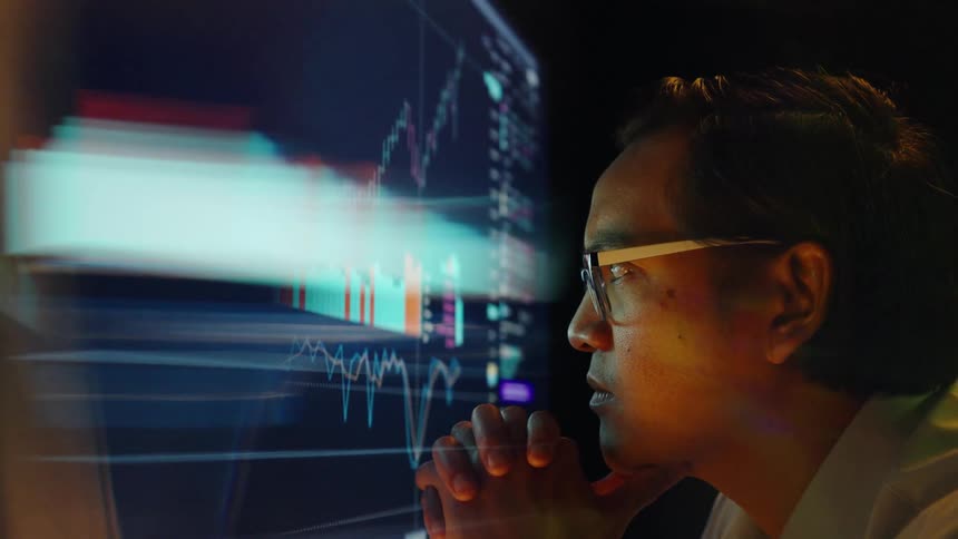 Young adult man wearing glasses and a white dress shirt looking at candlewick pattern charts on a blurred screen indoors