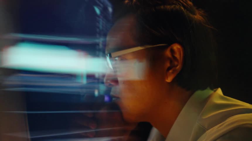 Man wearing glasses analyzes financial charts on a large screen