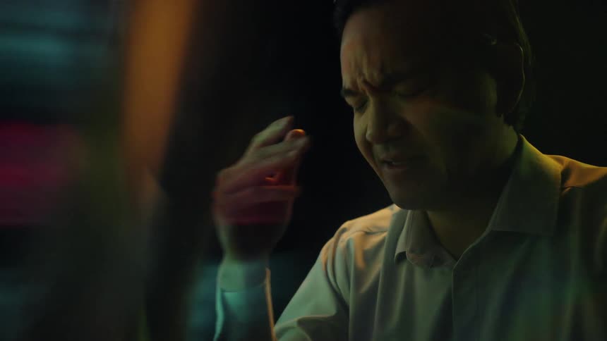 Adult man wearing glasses and a dress shirt touching his face with a nervous facial expression in front of a screen indoors