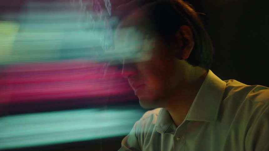 Man pressing the bridge of his nose in front of a screen with charts and numbers