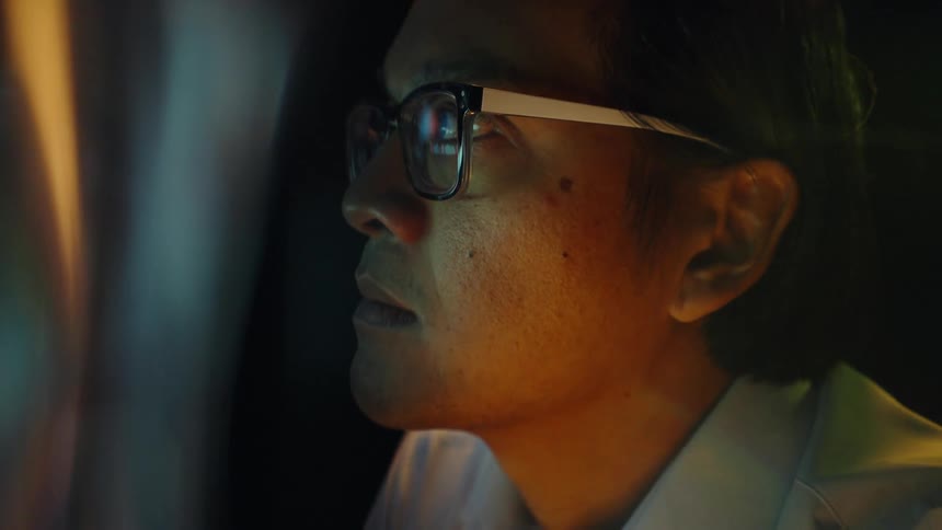 A man with glasses and a white shirt stares intently at a glowing digital screen displaying colorful financial charts and data visualizations within a dark room