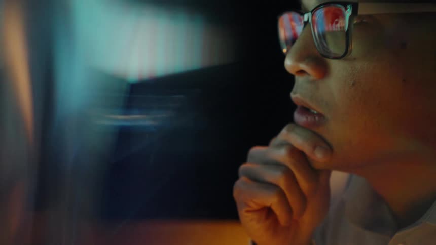 Man wearing glasses looks at a screen with his hand resting on his chin