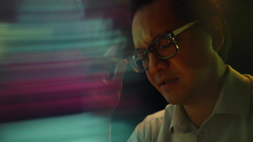 The man takes off his glasses in front of the monitor